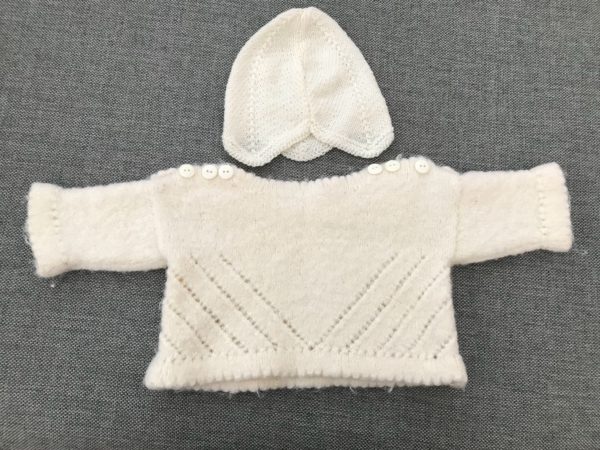 vit stickad tröja med 3 vita knappar på vardera axel, som passar bebisar 0-3 månader, matchande mössa ingår